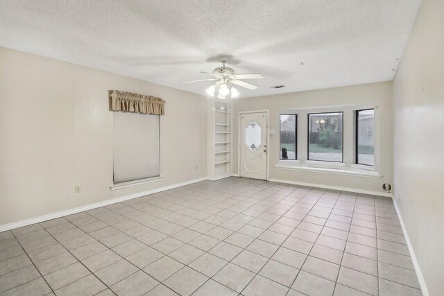 empty room with ceiling fan, a textured ceiling, built in shelves, baseboards, and visible vents