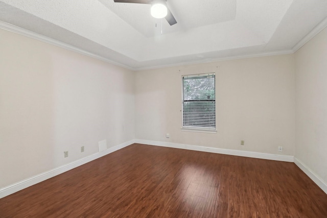 spare room featuring a ceiling fan, dark wood-style flooring, baseboards, ornamental molding, and a tray ceiling