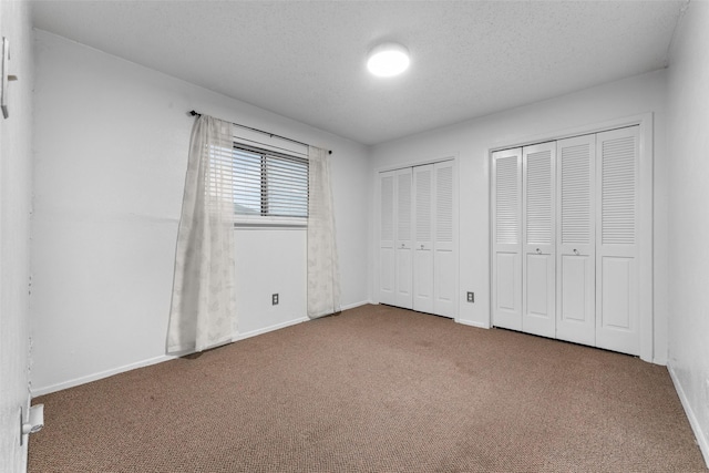 unfurnished bedroom featuring baseboards, carpet flooring, a textured ceiling, and two closets