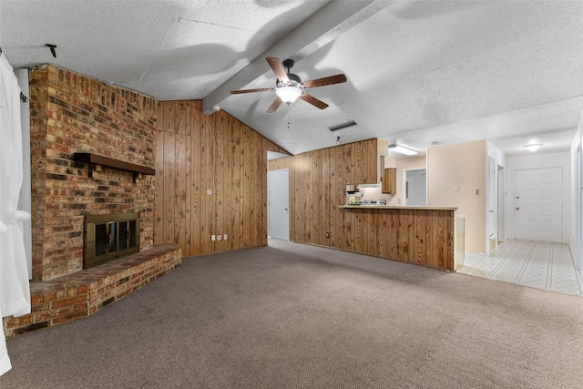 unfurnished living room featuring visible vents, wood walls, light carpet, ceiling fan, and lofted ceiling with beams