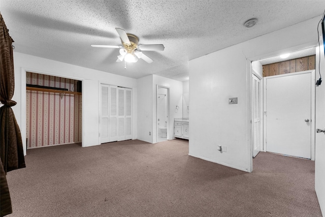 unfurnished bedroom with connected bathroom, ceiling fan, carpet floors, a textured ceiling, and multiple closets