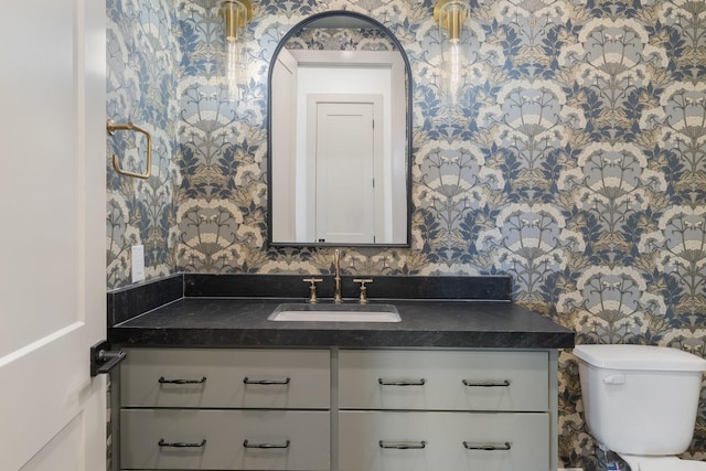 bathroom with vanity, toilet, and wallpapered walls