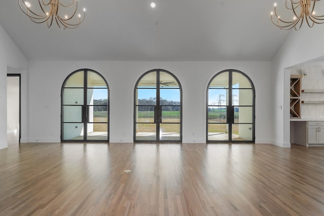 unfurnished living room with baseboards, light wood-style flooring, a chandelier, and vaulted ceiling