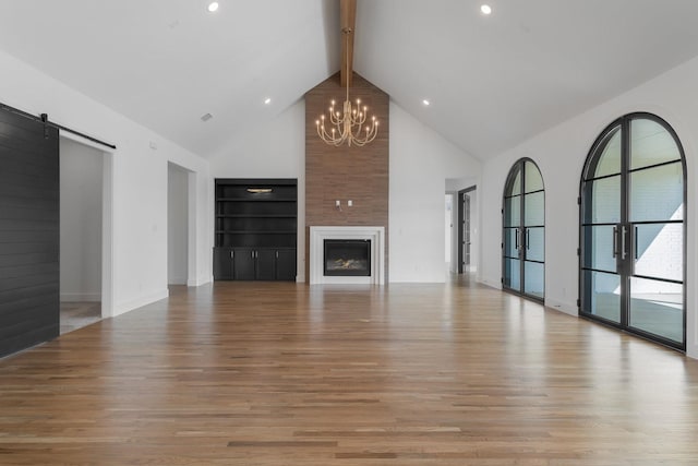 unfurnished living room with a notable chandelier, a barn door, light wood-style floors, high vaulted ceiling, and beamed ceiling