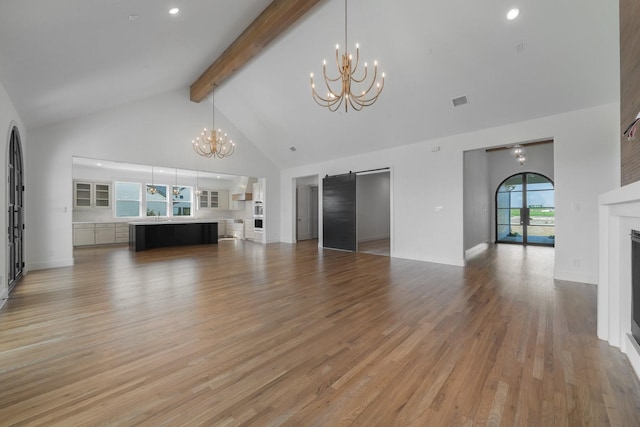 unfurnished living room featuring a notable chandelier, beam ceiling, a fireplace, high vaulted ceiling, and light wood-type flooring