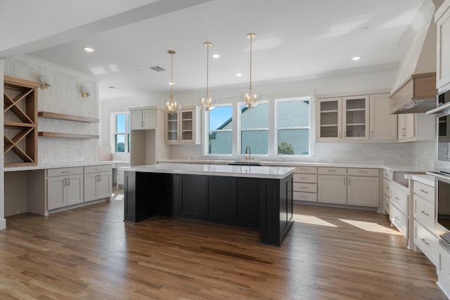 kitchen featuring glass insert cabinets, a center island, a sink, backsplash, and a notable chandelier