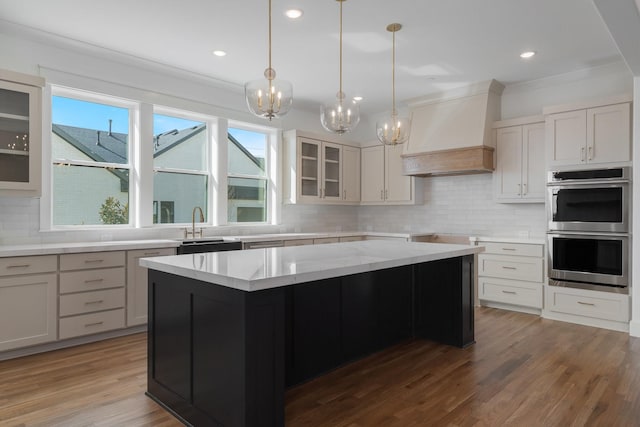 kitchen featuring an inviting chandelier, decorative backsplash, custom exhaust hood, stainless steel double oven, and light stone counters