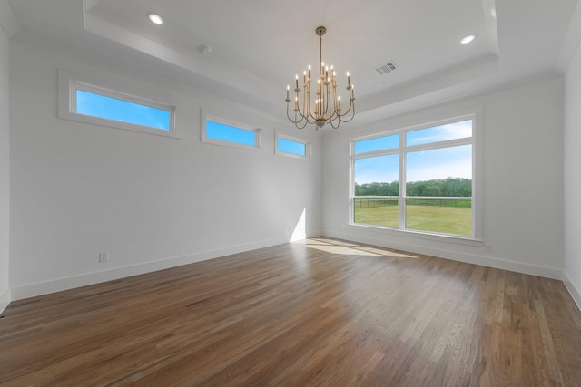 unfurnished room featuring a raised ceiling, a notable chandelier, wood finished floors, and visible vents
