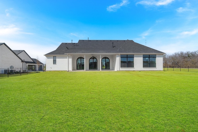 back of property with a lawn, a shingled roof, and fence