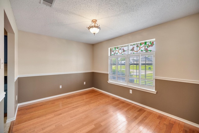spare room featuring baseboards, a textured ceiling, visible vents, and wood finished floors