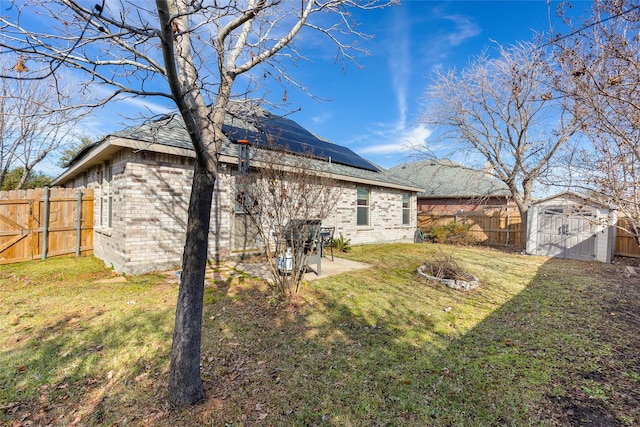 rear view of house featuring brick siding, roof mounted solar panels, a fenced backyard, a storage unit, and a yard