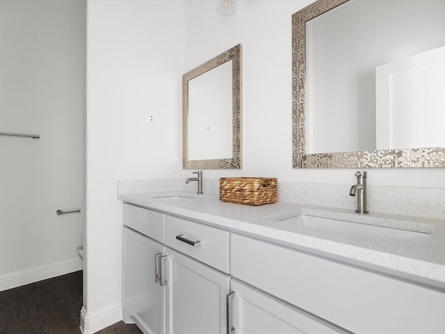 full bathroom with double vanity, a sink, baseboards, and wood finished floors