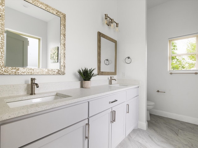 full bathroom featuring double vanity, a sink, baseboards, and toilet