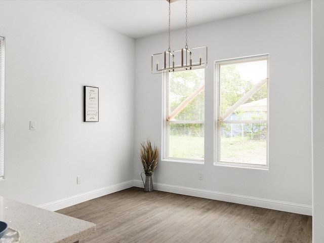 unfurnished dining area with baseboards, an inviting chandelier, and wood finished floors
