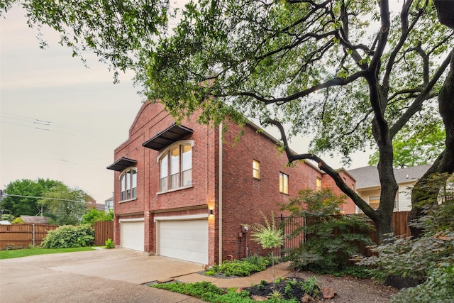 view of side of property with fence, an attached garage, concrete driveway, and brick siding