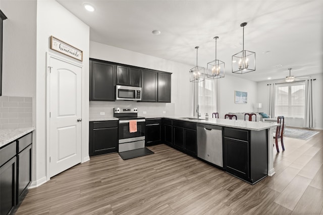 kitchen with decorative backsplash, light wood-style floors, open floor plan, a sink, and stainless steel appliances