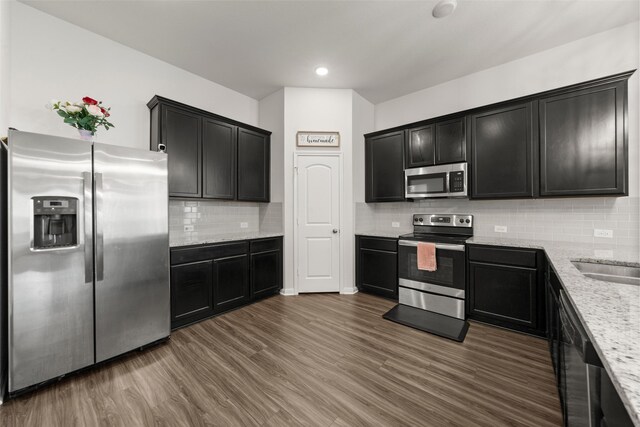 kitchen featuring dark wood-style flooring, dark cabinets, light stone countertops, and appliances with stainless steel finishes