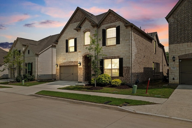 french country style house featuring brick siding, a garage, stone siding, and concrete driveway