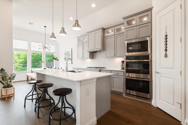 kitchen with stainless steel double oven, a center island with sink, gas stovetop, gray cabinetry, and a sink