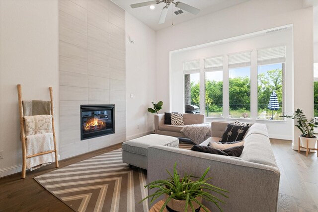 living room with a tiled fireplace, baseboards, ceiling fan, and dark wood-style floors