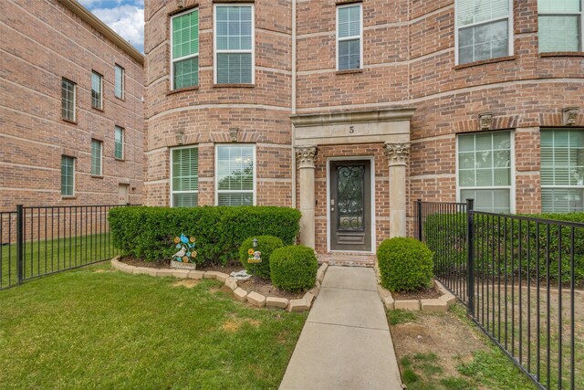 property entrance with brick siding, fence, and a yard