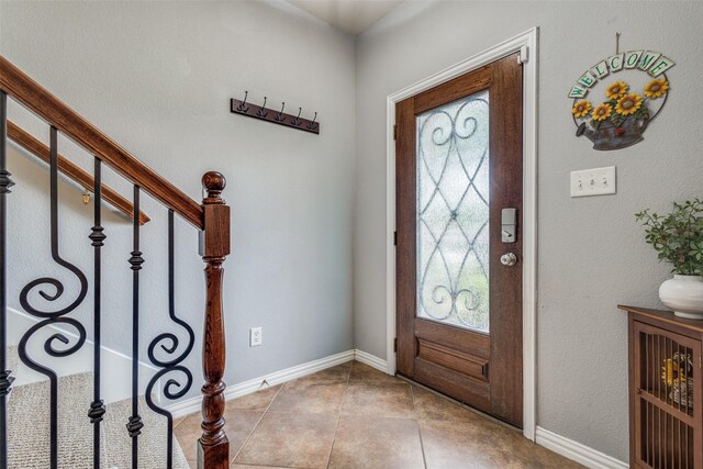 tiled entrance foyer featuring baseboards and stairway