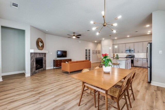 dining area with visible vents, baseboards, a tile fireplace, light wood-style flooring, and ceiling fan with notable chandelier