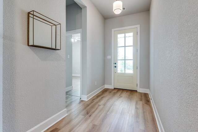 doorway with baseboards, a textured wall, and wood finished floors
