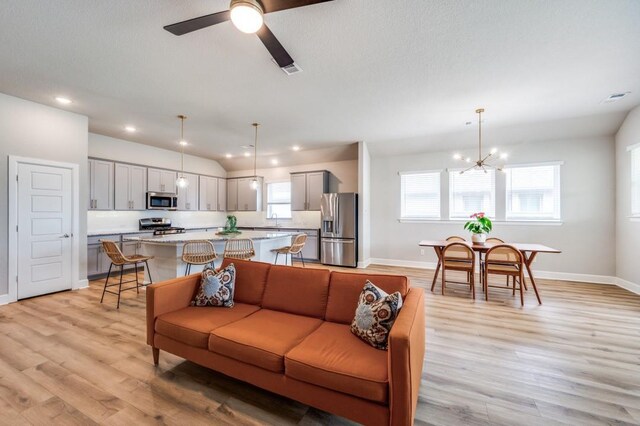 living area with baseboards, visible vents, light wood-style flooring, and ceiling fan with notable chandelier