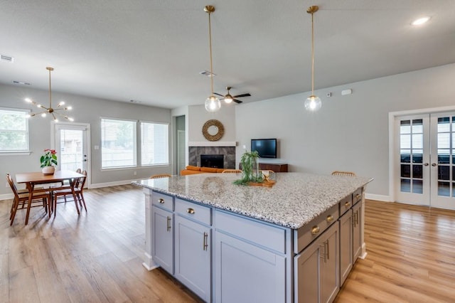 kitchen featuring light wood-style floors, a fireplace, ceiling fan with notable chandelier, and a wealth of natural light
