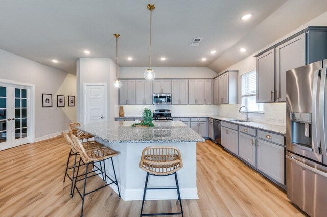 kitchen with a kitchen breakfast bar, visible vents, appliances with stainless steel finishes, gray cabinetry, and light wood finished floors