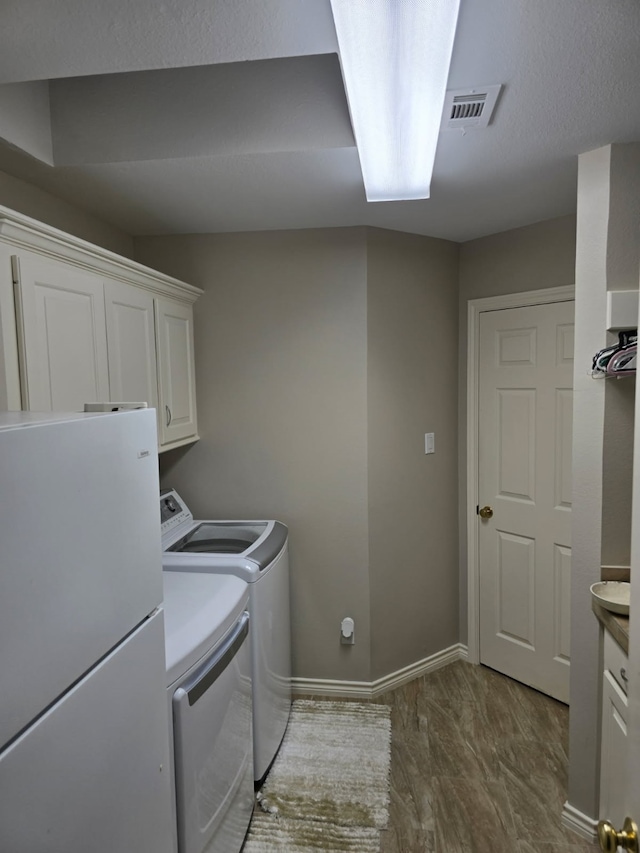 washroom featuring washer and dryer, cabinet space, baseboards, dark wood-type flooring, and visible vents