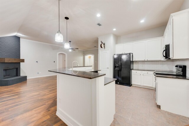 kitchen with a brick fireplace, an island with sink, white cabinetry, tasteful backsplash, and black appliances