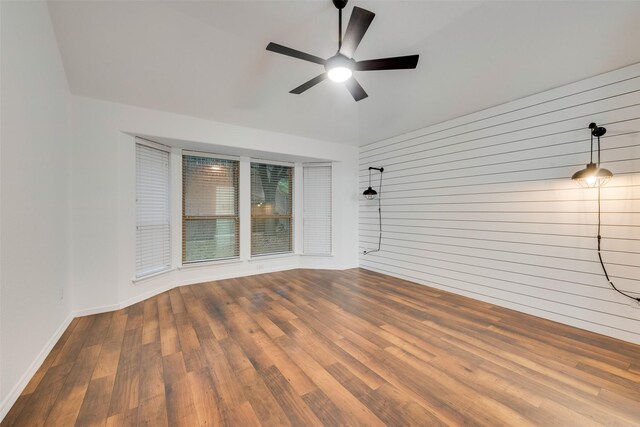 empty room featuring baseboards, ceiling fan, wood walls, and wood finished floors