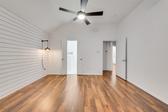 empty room with wooden walls, ceiling fan, baseboards, wood finished floors, and lofted ceiling