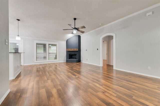 unfurnished living room with crown molding, a brick fireplace, wood finished floors, arched walkways, and a ceiling fan