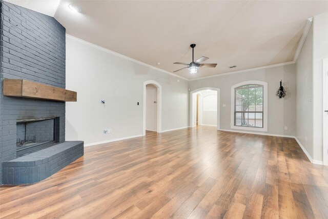 unfurnished living room with a brick fireplace, wood finished floors, baseboards, ceiling fan, and arched walkways