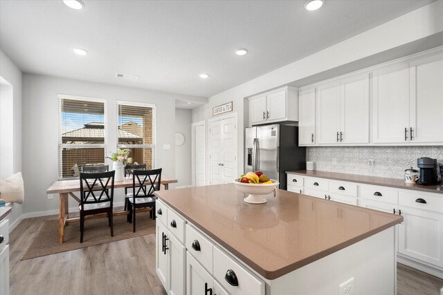 kitchen featuring visible vents, a center island, white cabinets, stainless steel fridge, and light wood-style flooring
