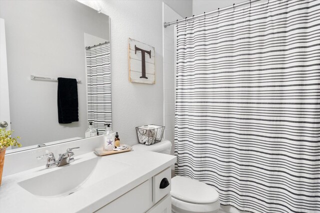 full bath featuring vanity, a textured wall, curtained shower, and toilet