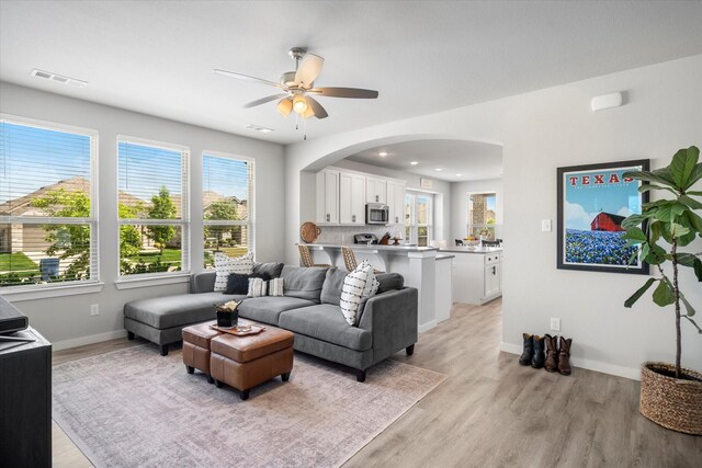 living room featuring light wood finished floors, arched walkways, a ceiling fan, baseboards, and visible vents