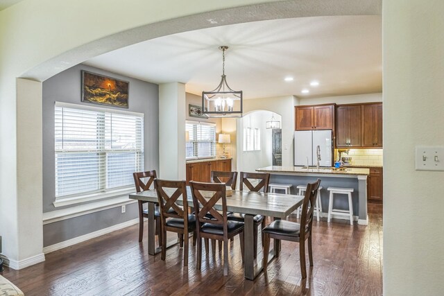 dining space with arched walkways, baseboards, dark wood-style flooring, and a notable chandelier