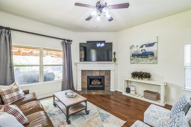 living area with plenty of natural light, a tiled fireplace, ceiling fan, and wood finished floors