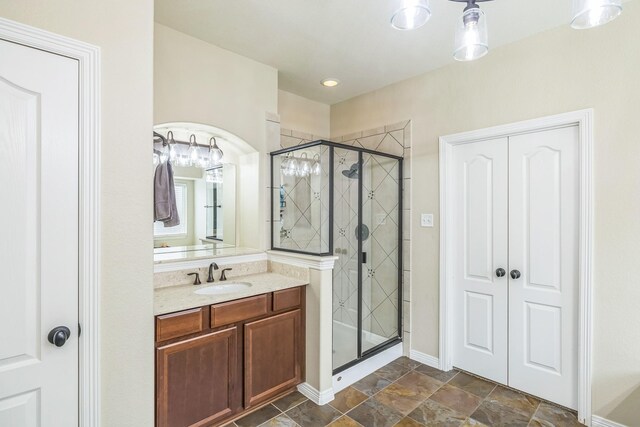 full bathroom with vanity, baseboards, a stall shower, and stone finish floor