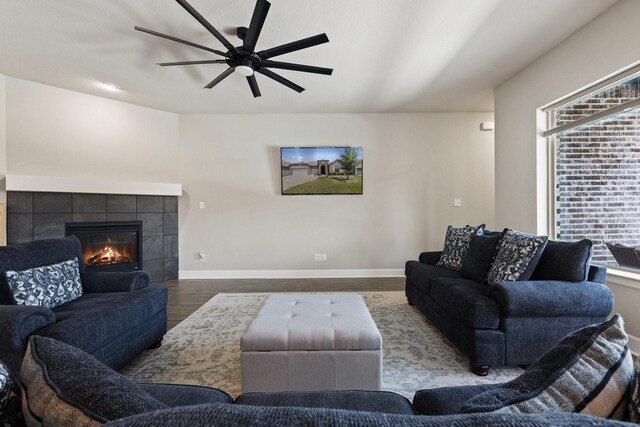 living area featuring a ceiling fan, baseboards, wood finished floors, and a fireplace