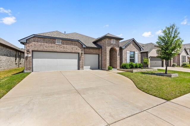 french country home featuring a front yard, roof with shingles, brick siding, concrete driveway, and an attached garage