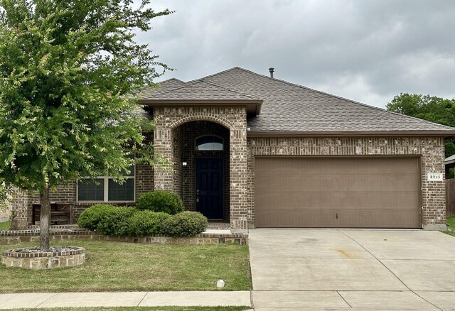 view of front of home with a front yard, roof with shingles, a garage, brick siding, and concrete driveway