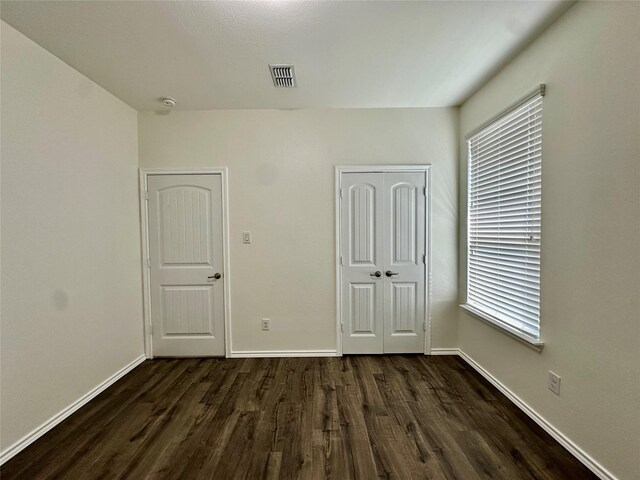 unfurnished bedroom featuring dark wood-type flooring, baseboards, and multiple windows