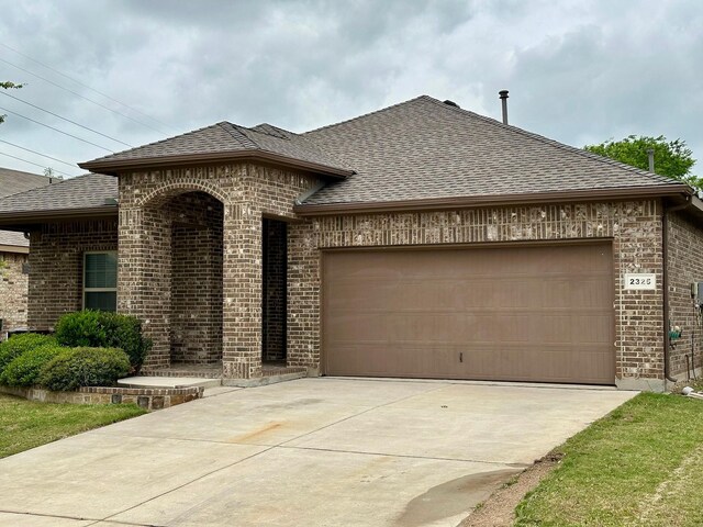 french provincial home with a shingled roof, driveway, and brick siding