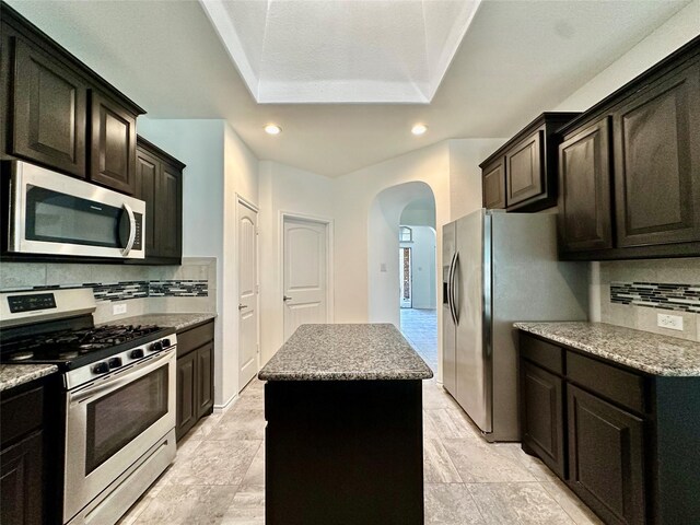 kitchen featuring backsplash, appliances with stainless steel finishes, a center island, arched walkways, and recessed lighting