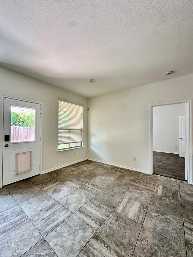 unfurnished room with a textured ceiling, baseboards, and a healthy amount of sunlight